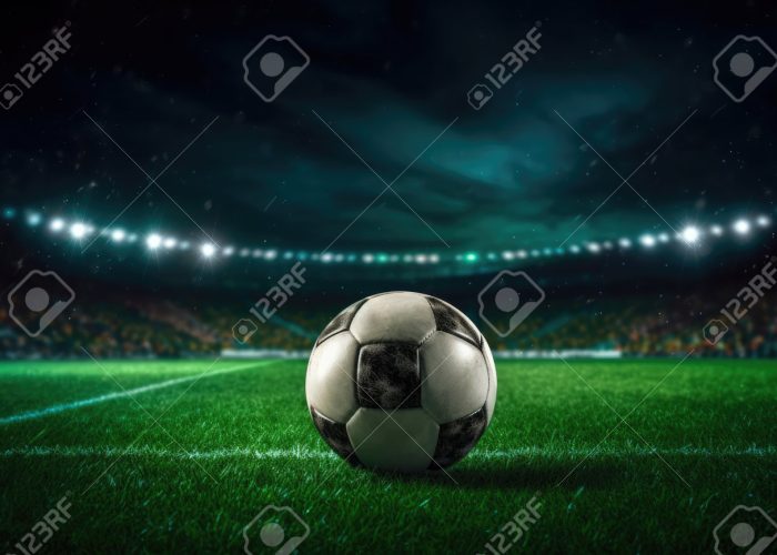 206684247-football-ball-on-the-grass-of-a-football-field-lights-on-the-stadium-at-night
